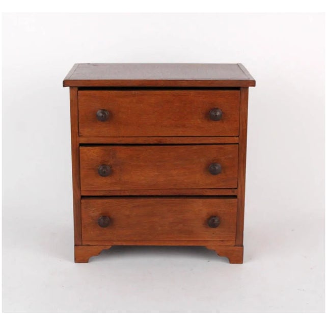 A small, plain Federal style oak chest of three drawers in a warm honey-brown finish with a plain overhanging top, simple...