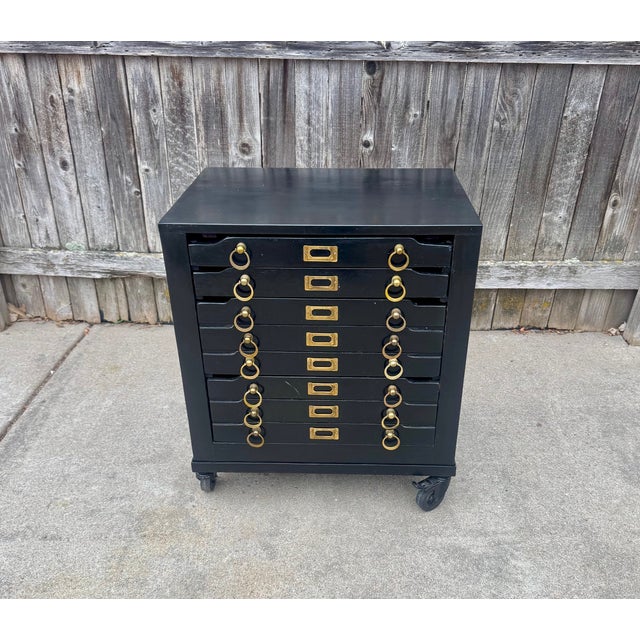 Printmakers nightstand in vintage mango with a black finish and brass hardware, rising on locking casters. Two narrow...