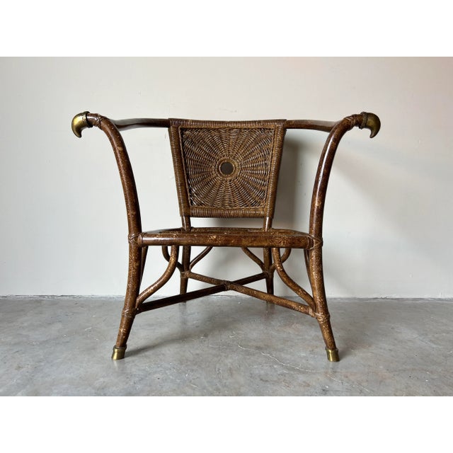 A distinctive organic modern armchair featuring rattan frame with open arms and woven wicker back with brass details on...