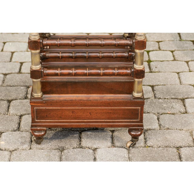 An English mahogany magazine rack on casters from the mid-20th century, with faux bamboo accents, two drawers and brass...
