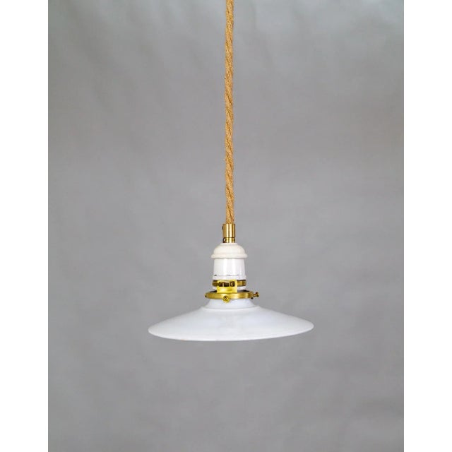 A contemporary pendant light with a rope-covered cord, small milk glass saucer shade, and ceramic and brass canopy....