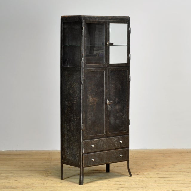 Antique metal cabinet with a robust, industrial aesthetic and a beautifully weathered patina. The unit features glass...