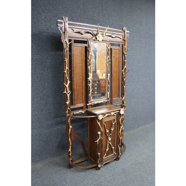 Adirondack style oak hall rack with mounted deer antlers. Vertical back with central mirror, shelf, and lower cabinet....