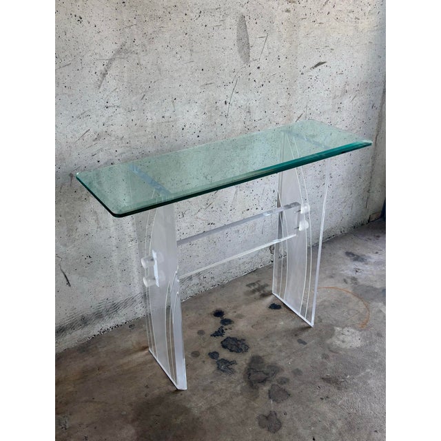 A sleek and timeless mid-century console table featuring a sculptural lucite base topped with thick beveled glass. The...