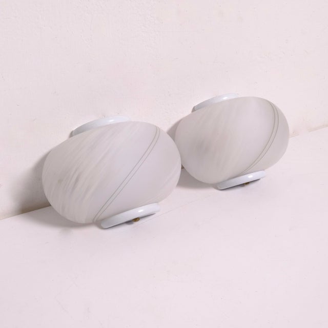 Simple and elegant pair of wall lights in white Murano glass on white metal frames, with tone-on-tone decoration....