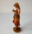 Detailed carved wooden figure of a barefoot girl absorbed in an open book, with a basket hanging from her arm. Her braided...