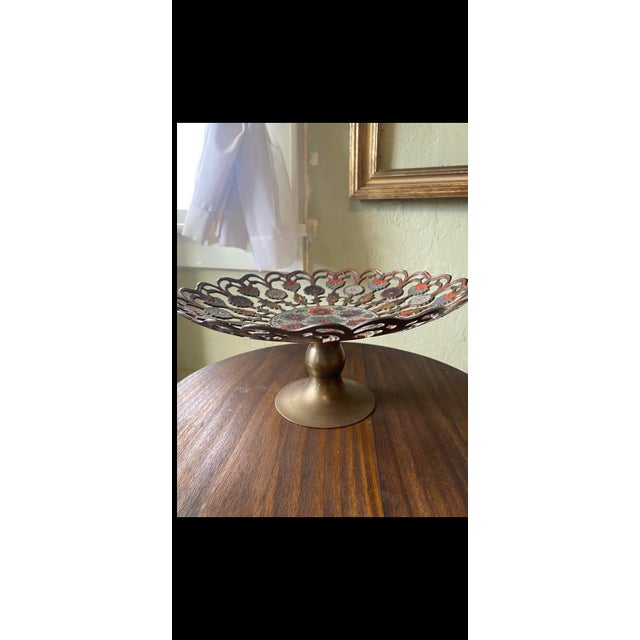 This decorative bowl features intricate enamel cutouts and a scalloped edge. Do not use for food consumption. Aged Brass...
