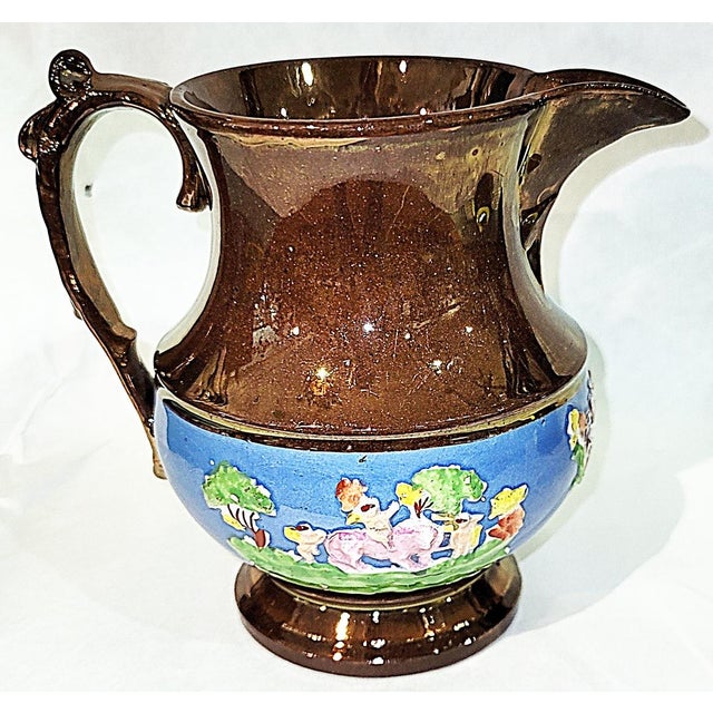 Tall pitcher from the UK, c 1920-30s in copper lustrewear, a metallic overglaze, nice riased decorative scene on the...