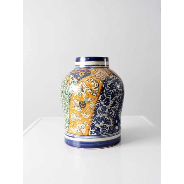 A vintage Talavera-style pottery vase featuring a classic urn silhouette and richly detailed hand-painted decoration. The...