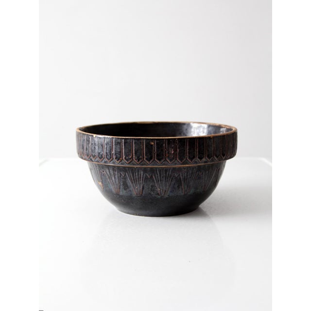 A late 19th century stoneware bowl with a deep, dark glaze and incised geometric banding along the rim and body. The...