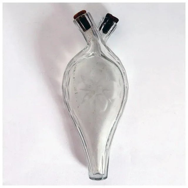 An antique bottle of flattened teardrop shape with twin flasks and spouts with cork stoppers. Etched with a flowerhead....