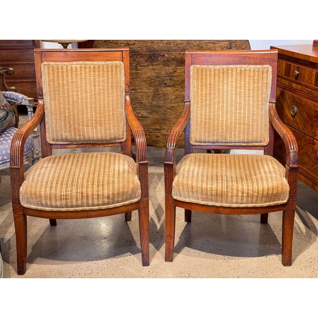Handsome near pair of Empire style open-arm chairs with square backs and fluted, carved arm supports. Upholstered in...