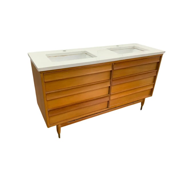 Striking Mid-Century Modern dresser professionally repurposed as a double-sink bathroom vanity. The warm wood cabinet...