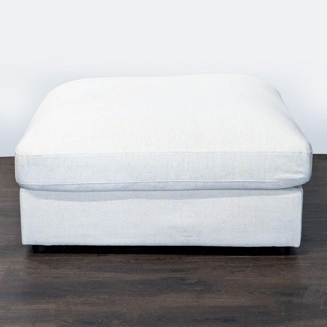 This modern square ottoman features a soft light beige fabric and a thick cushioned top, making it perfect for use as...