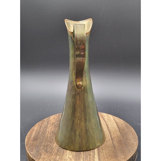 This is an antique Russian hammered brass pitcher, featuring a copper rim and handle. This decorative ewer is known for...