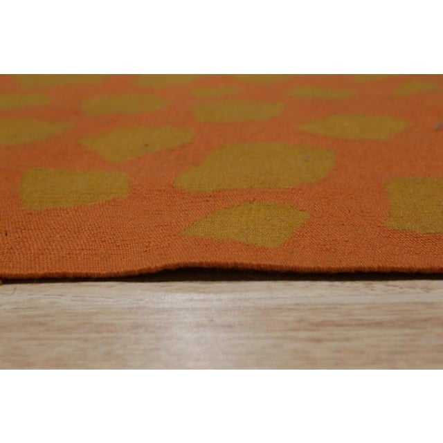 This handmade flat weave rug features a primary color palette of coral, salmon, and pink tones crafted from durable wool....