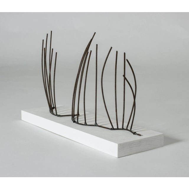 Iron sculpture with a rusted finish by Fred Leyman, mounted on a wooden base. The iron strands bring grass blowing in the...