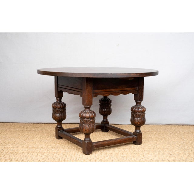 A low, round oak table, Spanish Revival style, c. 1930, American. Featuring a dark stained finish, a square base with cup...
