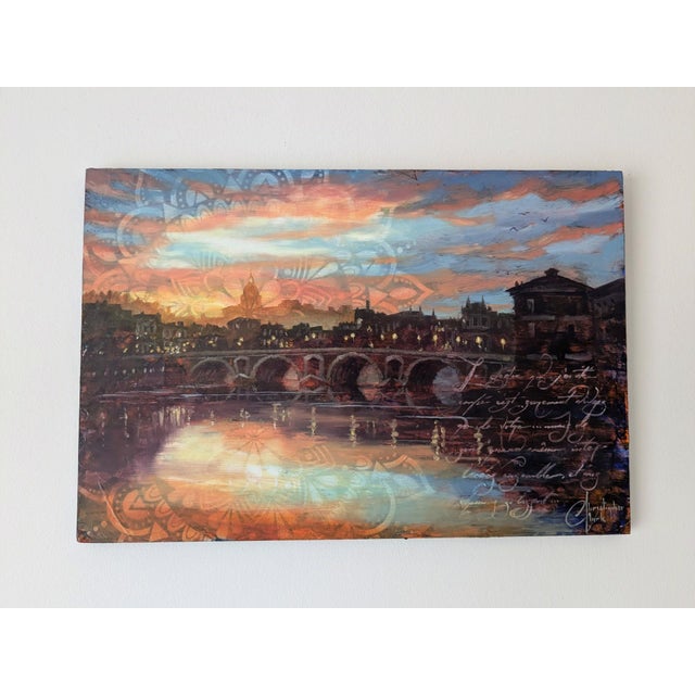 This artwork depicts a serene sunrise over the Pont Neuf in Toulouse, with warm hues reflecting on the water's surface....