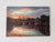 This artwork depicts a serene sunrise over the Pont Neuf in Toulouse, with warm hues reflecting on the water's surface....