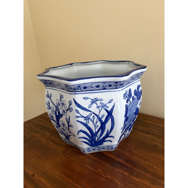 A classic blue and white porcelain planter, rendered in a softly faceted, scalloped form that feels both tailored and...