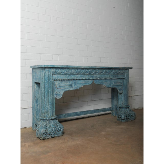 A wooden console table with a sculptural presence, defined by carved detailing and a weathered blue surface. The...