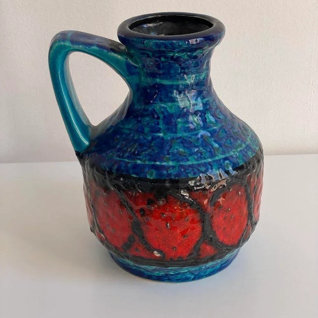 Glazed ceramic vase with jug motif in shades of blue, green, red, and brown. Not water-tight.