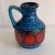 Glazed ceramic vase with jug motif in shades of blue, green, red, and brown. Not water-tight.