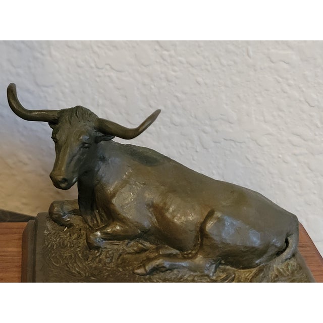 A finely small cast bronze sculpture of a reclining longhorn steer, mounted on a solid wood base with a brass nameplate...