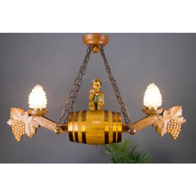 This interesting and unusual hand-carved wooden chandelier features a centered large wine barrel and a wooden figurine of...