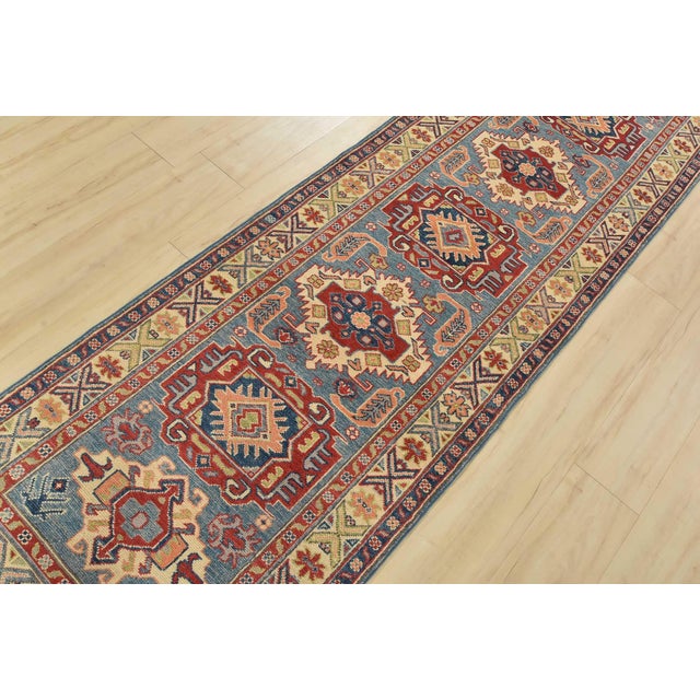 A tribal Caucasian Kazak runner hand-knotted with fine wool on a cotton foundation. This rug features a row of geometric...