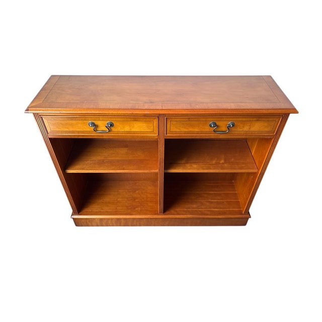 Compact English bookcase in yew wood with two drawers and open shelving. Classic design with brass handles and a warm,...