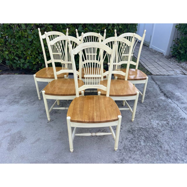 A set of six dining chairs. Each chair has a crème colored frame with a wood seat French Countryside / Cottage Style Sheaf...