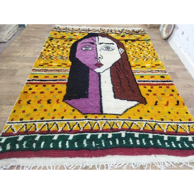 A striking Moroccan Berber wool textile featuring a bold abstract figurative portrait design, handwoven in the High Atlas...