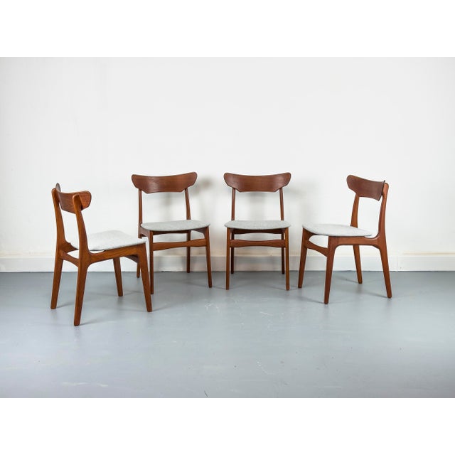 A set of four teak dining chairs with a delicate, organic frame and upholstered seats, newly reupholstered in light gray...