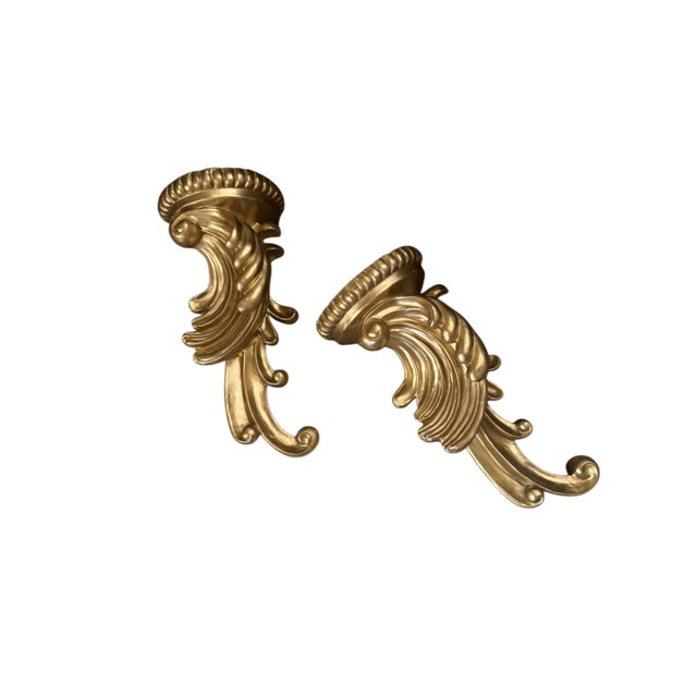 A striking pair of substantial gilt wall sconces featuring deeply sculpted acanthus leaves, scrolling flourishes, and...