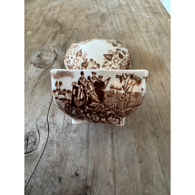 A charming miniature covered dish featuring classic brown transferware decoration on a creamy white ceramic ground. The...