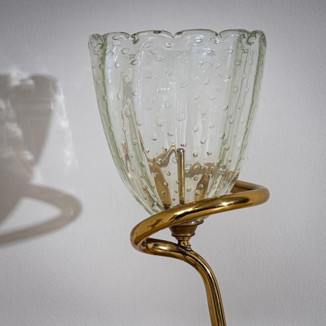 Small table lamp featuring a gracefully twisted brass base and a petite flower-shaped glass shade. The hand-blown glass...