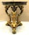 The Maitland Smith Egyptian Revival Table with Winged Creatures and Brass Claw Feet from the 1980s is a round accent table...