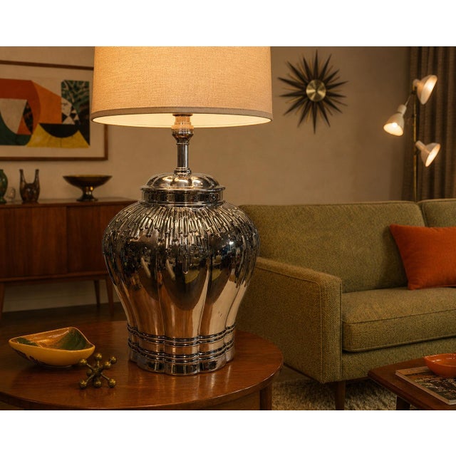 A large urn-shaped table lamp made of reflective silver mercury glass featuring fluted and lobed decorations with a...