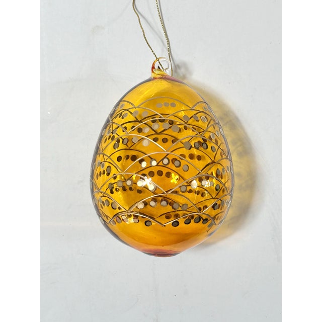 Vintage blown glass egg ornament in a rich, translucent amber color, decorated with an intricate pattern of overlapping...