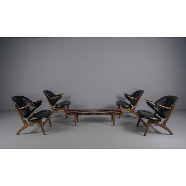 The wide, concave backrest forms on the side of the armrests that protrude forward like wings and enclose the seating. The...