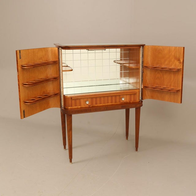 An elegant bar cabinet featuring beautifully figured flame mahogany veneer. The doors open to reveal a mirrored interior,...