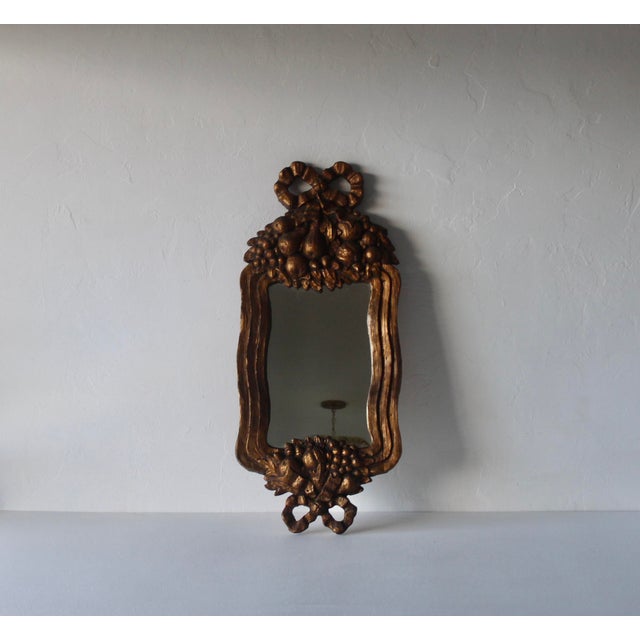 Ornate framed mirror with fruit and ribbon motifs typical of the Rococo period with antique gold finish. Made with a mold...