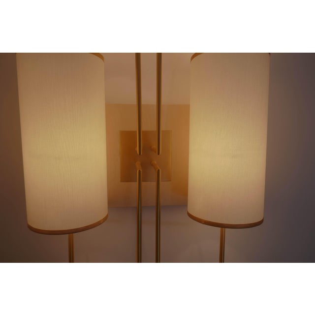 A wall light in patinated gold metal, with a sycamore base. The lampshades are white fabric with a gold trim. It hangs...