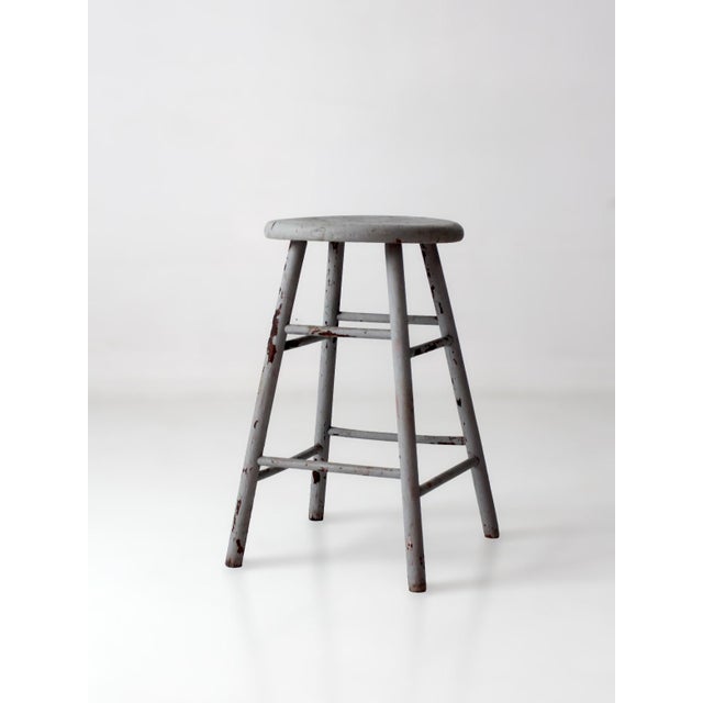 Antique wood stool with a round seat, splayed legs, and double-stretcher construction, finished in a softly weathered gray...