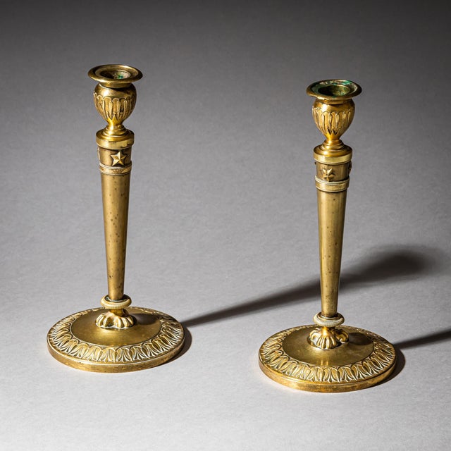 Pair of brass candle holders with circular disc bases decorated with a surrounding leaf frieze. Stylized claw feet and...