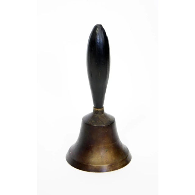 Vintage brass hand bell with a hand-carved, painted black wooden handle. The metal has a dark patina on the exterior...