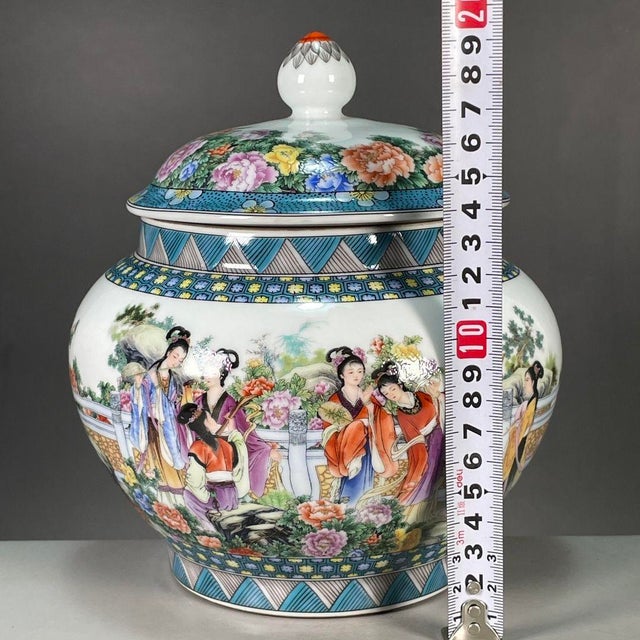 A vibrant Chinese porcelain covered jar decorated in colorful Famille Rose enamels. The white ground features a detailed...