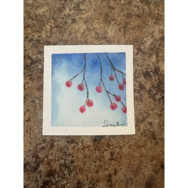 Soft red berries dangle from slender branches, set against a serene wash of pale blue. The subtle textures and restrained...